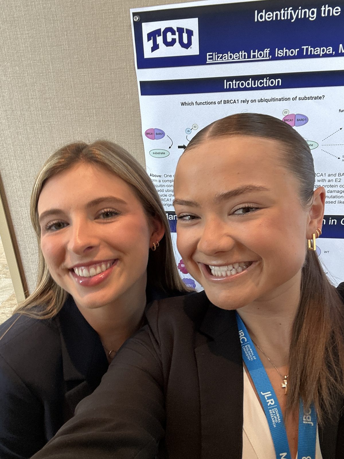Two lab members taking a selfie in front of a research poster