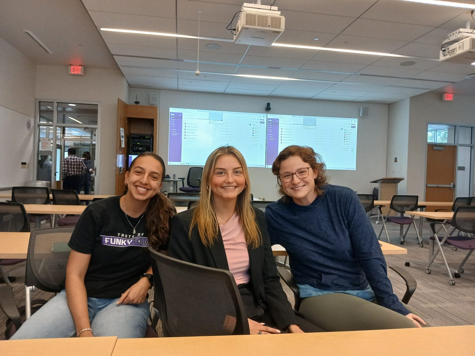 Three lab members in a classroom with data on the screens behind them